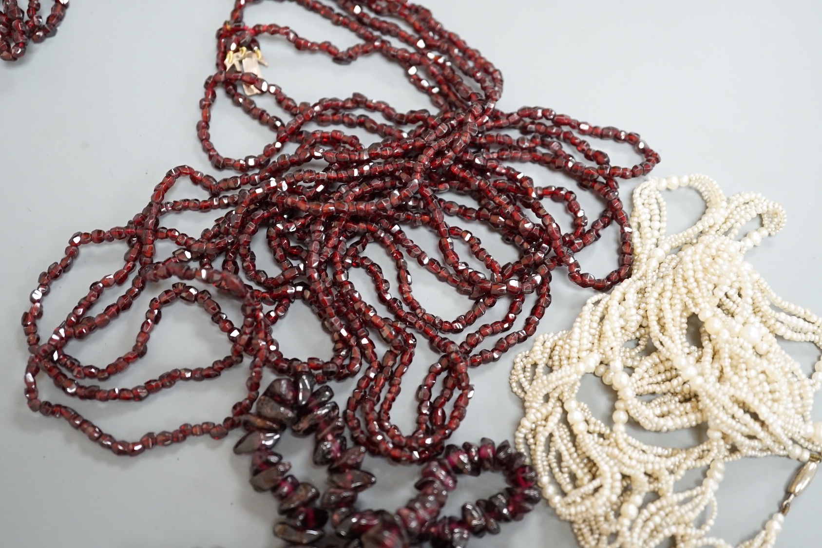 An early 20th century triple strand facet cut garnet necklace, with yellow metal clasp, 122cm, a similar single strand garnet 'pebble' necklace and a seed pearl necklace, 118cm.